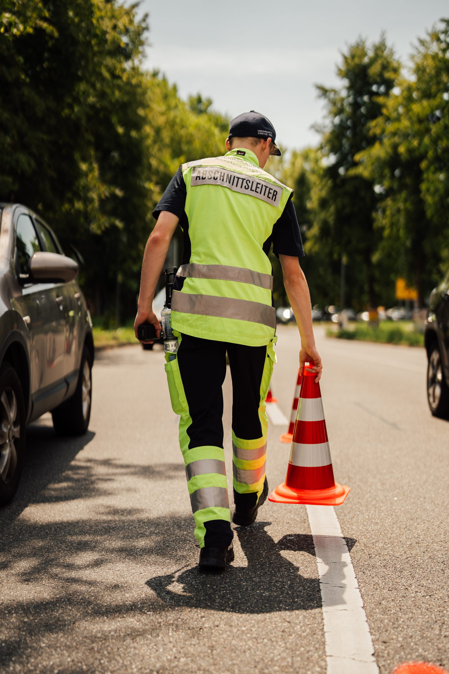 Verkehrskadett mit Funktionsschild stellt eine Pylone auf die Straße